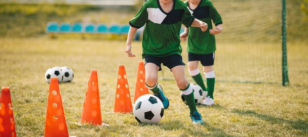 スラロームドリル中にトレーニングコーンの間にサッカーボールを実行してキック2人の学校の少年  - 写真・画像