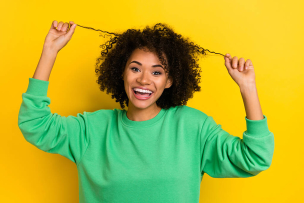 Photo of cheerful excited girl hands touch playing hair curls look camera isolated on yellow color background. - Foto, immagini