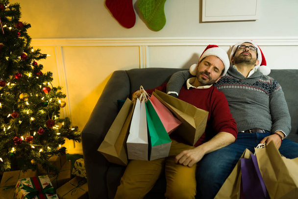 Moe gay paar rusten op de bank met een heleboel winkelen tassen na thuiskomen van kopen kerstcadeaus - Foto, afbeelding