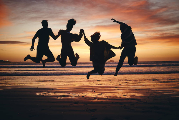 自由,ビーチでの友人のジャンプやシルエットや成功のためのブラジルの休暇に旅行,幸せや動機.夏、若さと楽しみのための日没の人々のチームワーク、コラボレーションと影. - 写真・画像