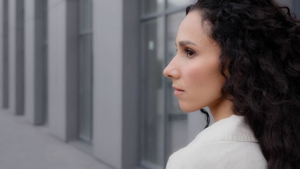 Close up back view Caucasian pensive thoughtful brunette lady with long curly hair looking away thinking dreaming pondering think waiting standing outdoors in city calm Latina Hispanic woman outside - Photo, Image