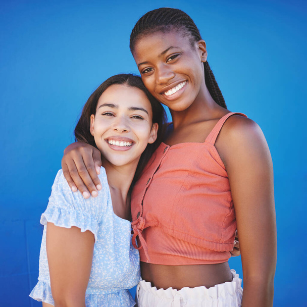 Mujeres negras, amigos y abrazos con sonrisa feliz en un fondo de estudio azul. Retrato, diversidad y pareja de lesbianas enamoradas abrazan, cuidan y apoyan posando, uniendo y pasando tiempo de calidad juntos - Foto, imagen
