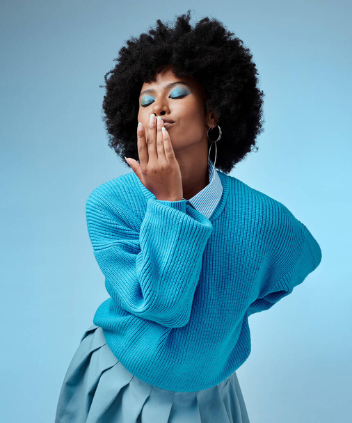Girl, blue and background with clothes for fashion with hand, face and kiss in studio with afro. Happy, model and fingers on lips for makeup, hair and beauty with azure color backdrop in Los Angeles. - Foto, imagen