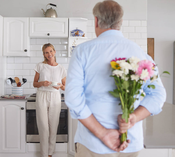 Elderly, couple and flowers in kitchen for surprise, love and romance in their house. Woman, man and retirement together with bouquet to celebrate marriage, birthday or anniversary in their home. - Foto, Bild