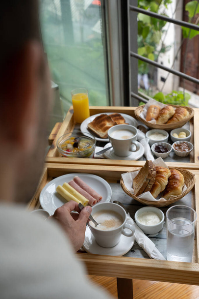 Неузнаваемый человек завтракает в гостиничном номере с вкусным полным американским сервисом завтрака.  - Фото, изображение