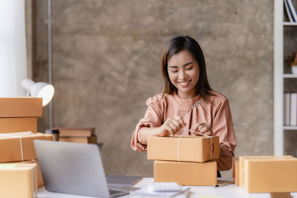 Online SME business and delivery concept, smiling girl, beautiful owner, Asian freelancer, online shopping SME business working on a laptop computer with parcel boxes on the table at home. - Foto, imagen