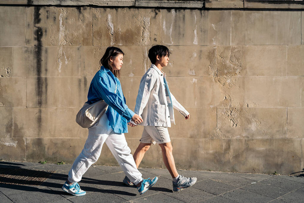 Cool asian couple walking in the city during sunny day and holding hands. - Фото, зображення