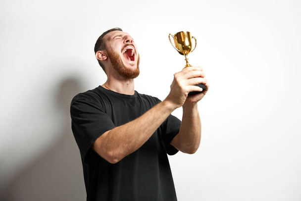 Happy young male or businessman holding his gold trophy and celebrating victory. Studio shot of man with cup as winner. Concept of win, success, human emotions, celebration, achievement, leadership - Fotografie, Obrázek