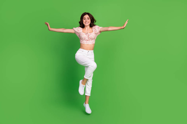 Full length photo of adorable cute girl dressed print blouse arms sides jumping high isolated green color background. - Foto, immagini