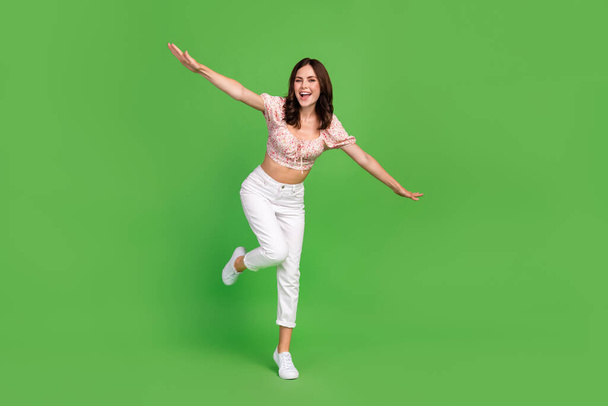 Full length photo of sweet good mood girl with curly hairdo wear white pants blouse running rejoice isolated on green color background. - Foto, afbeelding