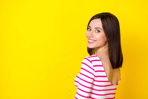 Фото красивої молодої чудової дівчини з боб-перукаркою, одягненою в смугасту сорочку, обертаються посміхаючись на камеру ізольовані на жовтому тлі
. - Фото, зображення