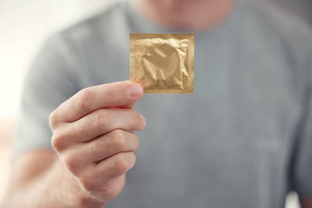Condom in man hand for safe sex, sexual safety and hiv awareness zoom. Person with male contraceptive product for sexual risk prevention, healthcare and caution for security, trust and love choice. - Photo, Image
