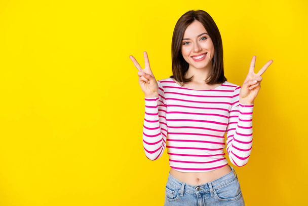 Photo portrait of cute young lady smiling show double v-sign empty space dressed stylish striped look isolated on yellow color background. - Foto, immagini
