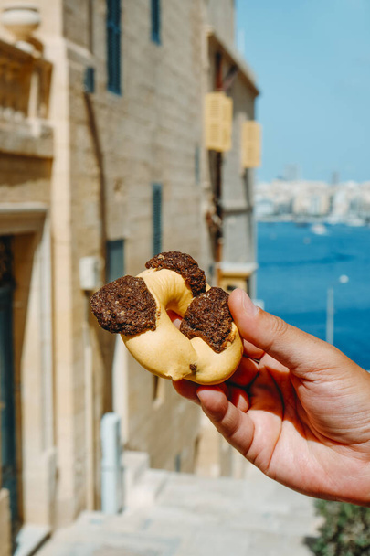 közelkép egy férfiról, aki egy qaghaq tal-ghaselt tart, más néven mézgyűrű angolul, tipikus Málta, az utcán Valletta óvárosában, Máltán, egy nyári napon - Fotó, kép