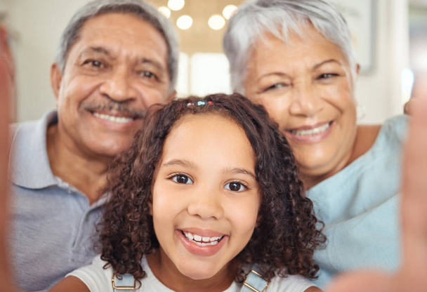 Szczęśliwi dziadkowie, dziewczęce dziecko robiące sobie selfie z parą seniorów i odwiedzające ich na emeryturze. Dzieciak uwielbia spędzać czas ze starszymi, dzielić się online z mediami społecznościowymi i cieszyć się razem jako rodzina. - Zdjęcie, obraz