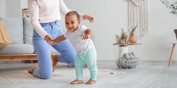 アフリカ系アメリカ人の母親が小さな赤ちゃんに家で歩くように教える - 写真・画像