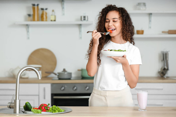 Молода афро-американська жінка споживає здоровий салат на кухні. - Фото, зображення