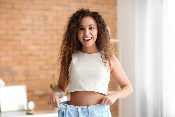 Happy young African-American woman in loose clothes at home. Diet concept - Zdjęcie, obraz