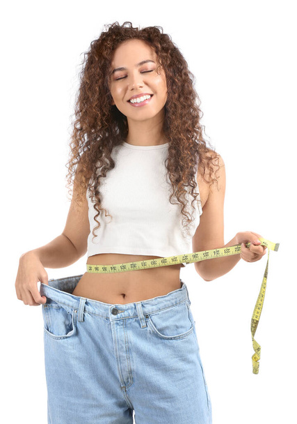 Happy young African-American woman in loose clothes and with measuring tape on white background. Diet concept - Photo, Image