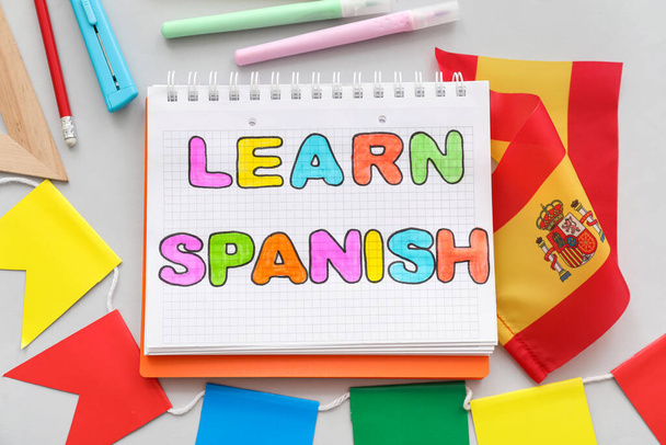 Notebook szöveggel LEARN SPANISH, zászló és írószer szürke alapon - Fotó, kép