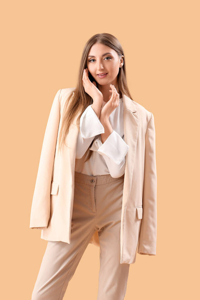 Beautiful fashionable young woman in elegant suit on beige background - Фото, зображення