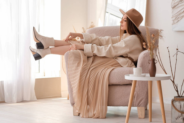 Gyönyörű divatos fiatal nő elegáns ruhákban ül karosszékben otthon - Fotó, kép