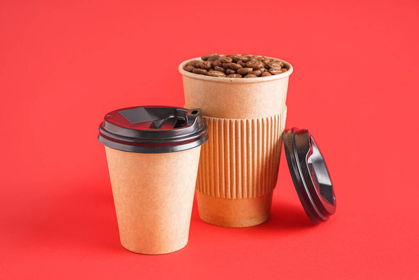Kırmızı arkaplanda kahve çekirdekleri olan kağıt bardaklar. - Fotoğraf, Görsel