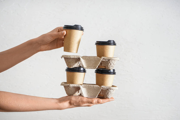 Woman holding holders with paper cups of coffee on light background - Φωτογραφία, εικόνα