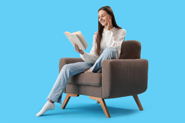 Beautiful woman reading book in armchair on blue background - Zdjęcie, obraz