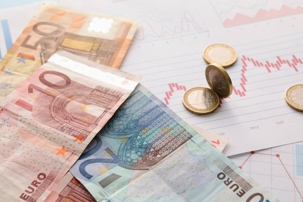 Euro banknotes with coins on diagrams, closeup. Exchange rate concept - 写真・画像