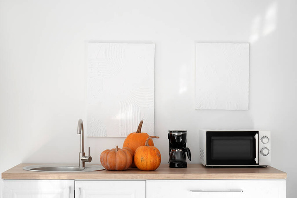 Кухонні лічильники з гарбузами на Хеллоуїн, кавоваркою та мікрохвильовою піччю біля світлої стіни
 - Фото, зображення