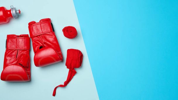Rode lederen bokshandschoenen, textiel handbeugel en waterfles. Sportuitrusting op een blauwe achtergrond - Foto, afbeelding