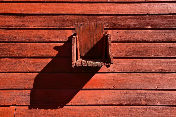 The outdoor chute to collect grain from a wooden red granary casts a long shadow. - Photo, Image