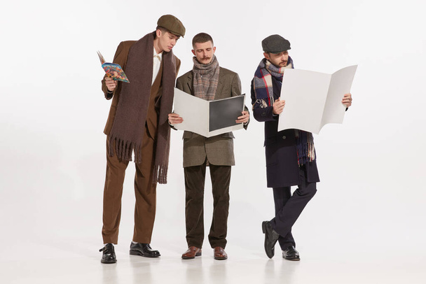 Portret van stijlvolle mannen die tijdschriften en kranten lezen geïsoleerd over grijze achtergrond. Herfst mannelijke mode. Concept van retro mode, stijl, vriendschap, creativiteit, jeugdcultuur, emoties, advertentie - Foto, afbeelding