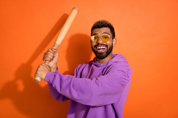 Portrait of cheerful nice person arms hold baseball bat toothy smile isolated on orange color background. - 写真・画像