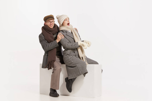 Portrait of cheerful young people, man and woman in winter clothes having fun together, sledding over white background. Concept of retro fashion, style, friendship, creativity, youth, emotions, ad - Zdjęcie, obraz