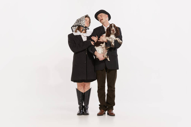 Портрет стильного молодого человека и женщины, пара, стоящая вместе с милой собакой на белом фоне студии. Концепция ретро моды, стиля, дружбы, творчества, молодежной культуры, эмоций, рекламы - Фото, изображение