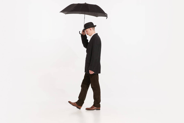 Portrait of stylish man in brown suit walking under umbrella isolated over white studio background. Concept of retro fashion, style, vintage, character, creativity, youth culture, emotions, ad - Fotoğraf, Görsel