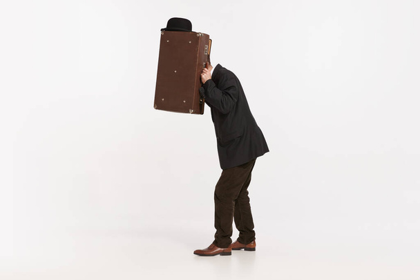 Ritratto di uomo elegante in abito marrone che copre il viso con valigetta isolata su sfondo bianco da studio. Concetto di moda retrò, stile, annata, carattere, creatività, cultura giovanile, emozioni, annuncio - Foto, immagini