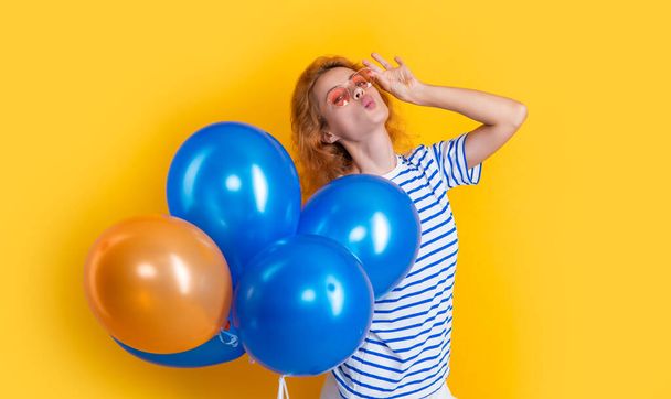 party girl with balloon in sunglasses. smiling girl hold party balloons in studio. girl with balloon for party isolated on yellow background. - Фото, изображение