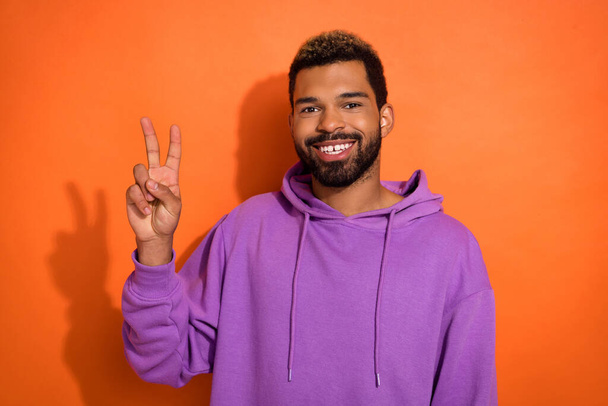 Photo of attractive funny boy man wear stylish purple clothes raise one hand arm show v sign isolated on orange color background. - Photo, Image