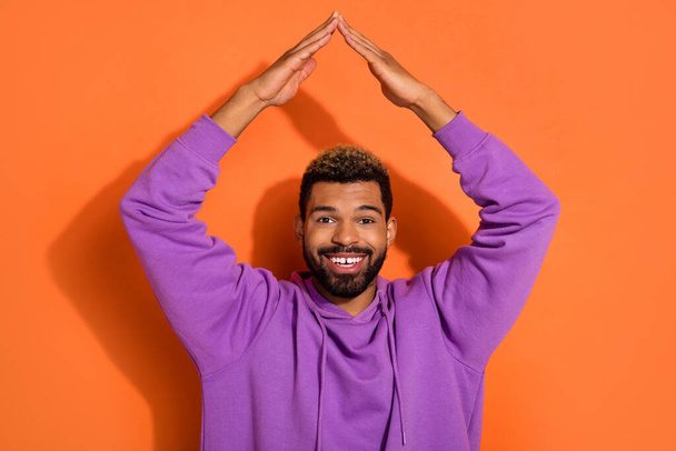 Photo of funky nice dude boy model stylish pullover hold arms over head make house roof isolated on orange color background. - Фото, зображення