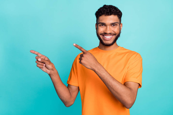 Photo of cute excited man dressed orange t-shirt smiling pointing two fingers empty space isolated turquoise color background. - 写真・画像