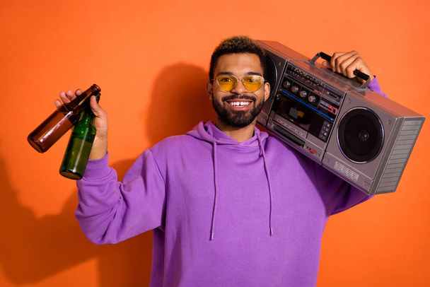 Portrait of cheerful carefree man carry boombox hold beer bottles isolated on orange color background. - Fotó, kép