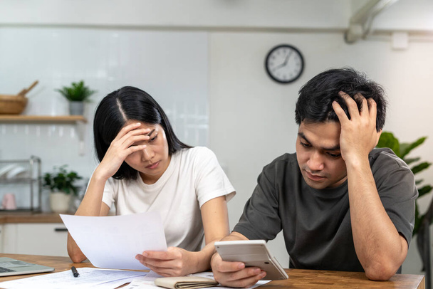 Asian couples are worried about debt and expenses. Stressful women and men receive bank loan invoices. credit card , water, electricity , telephone bills. No money and broke - Foto, Bild
