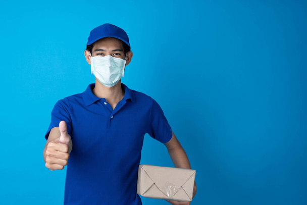 A futár kék egyenruhát visel. A feladó műtéti maszkot visel a pandémiás koronavírus fertőzés megelőzésére.. - Fotó, kép