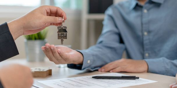 Broker nieruchomości wysyła klucze do domu do klienta po podpisaniu umowy z ubezpieczeniem. Hipoteka, wynajem, kupno, sprzedaż, przeniesienie koncepcji domu. - Zdjęcie, obraz