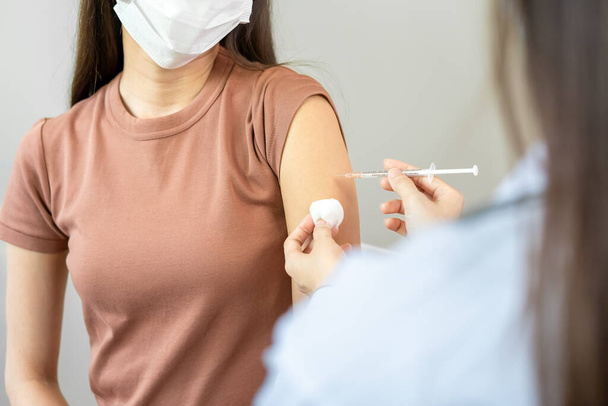 Asian woman wearing a medical mask receives coronavirus vaccine from a doctor. People are vaccinated against COVID-19 to prevent infection with the virus and stop its spread. - Photo, Image