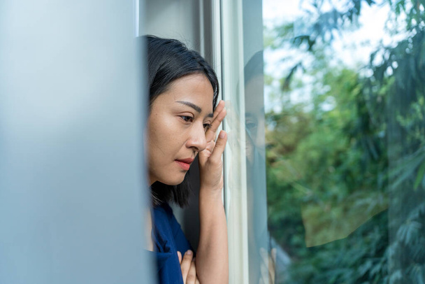 Красивая азиатка, разочарованная и грустная у окна. Стрессовая женщина путается с несчастливыми проблемами в жизни, спорит со своим парнем, случайно беременная. - Фото, изображение