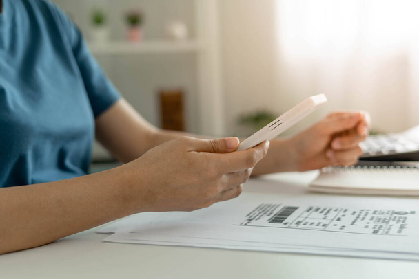 A woman uses a smartphone to scan the barcode to pay monthly phone bills after receiving an invoice sent to home. Online bill payment concept - Photo, image